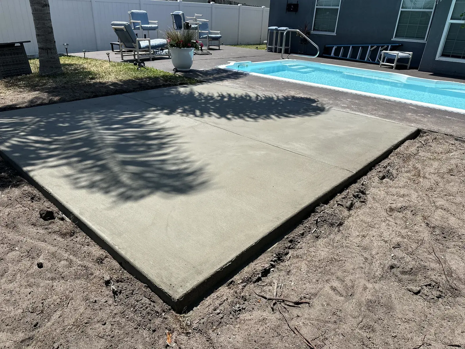 New concrete patio slab poured beside a backyard pool